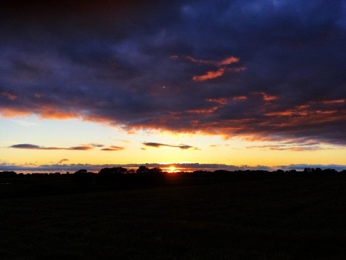 Dramatisk solnedgång med mäktiga moln och intensiva färger över ett landskap, tagen i november 2017.