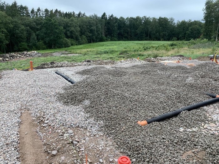 Byggplats med utspridd makadam, rörledningar och markerade områden i naturlig miljö.