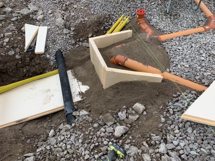 Byggprojekt med utspridd makadam, avloppsrör och isoleringsplattor i en grävd grund.