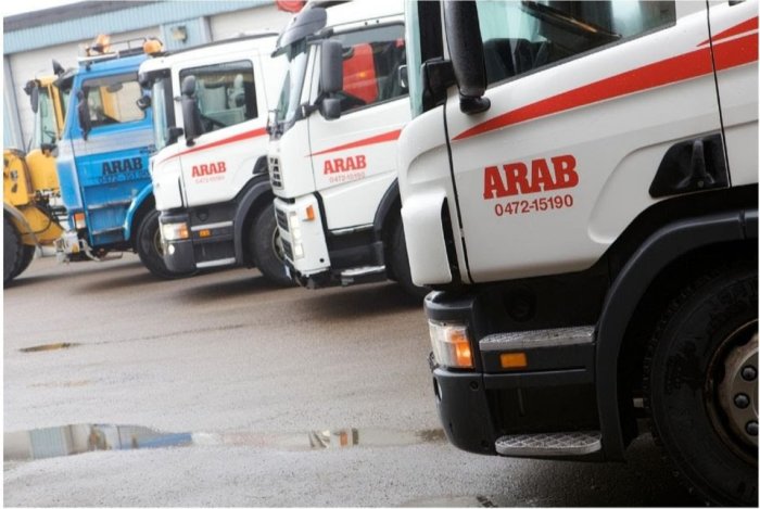 Lastbilar i rad med texten "ARAB" från Alvesta Renhållning AB på sidan, står parkerade på en våt asfalt.