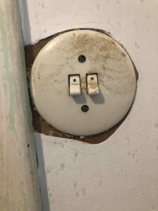 Rund ljusströmbrytare med två knappar på ojämnt monterad renoveringstapet.