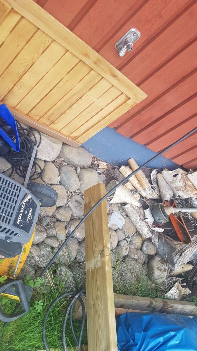 Byggplats med träreglar, kablar och byggmaterial nära en röd och gul trävägg, potentiellt för ett utekök eller bar.
