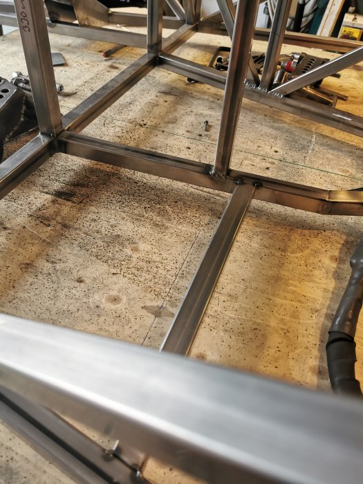 Robust metallramkonstruktion för pedalställ på en arbetsbänk i en verkstad.