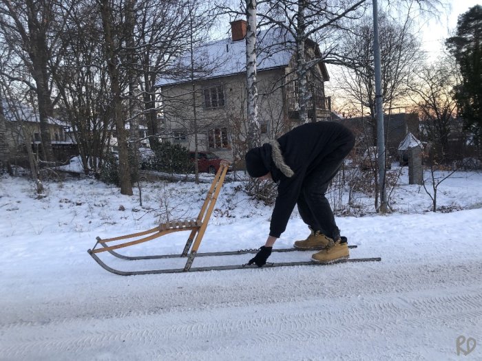 Person i svart jacka knyter fast sin sko på sparkstötting på en snötäckt väg.