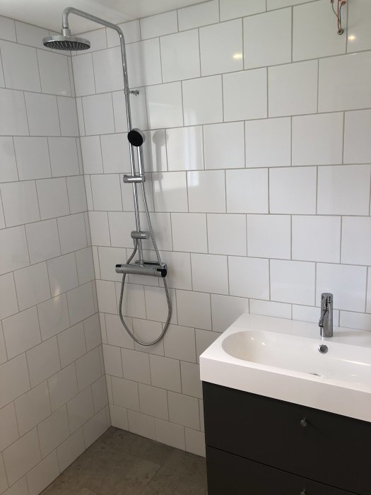Nästan färdigt badrumsrenovering med duschhörna, handfat och vita kakelväggar, saknar spegel och duschvägg.