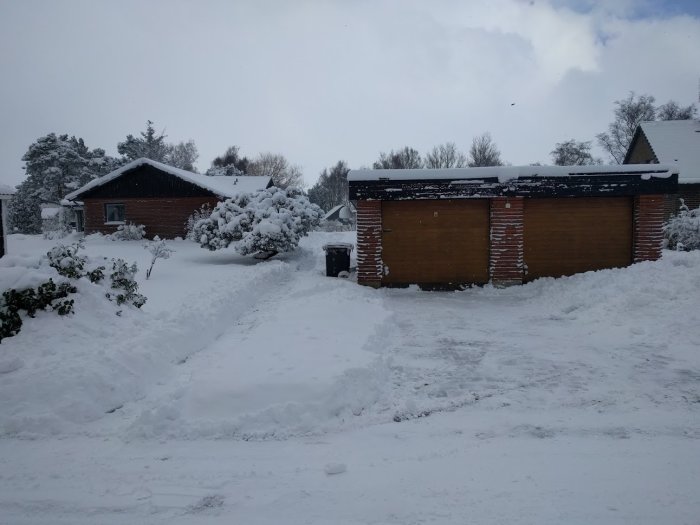 Vinterlandskap med ett hus och garage täckt av snö med spår efter snösläde.