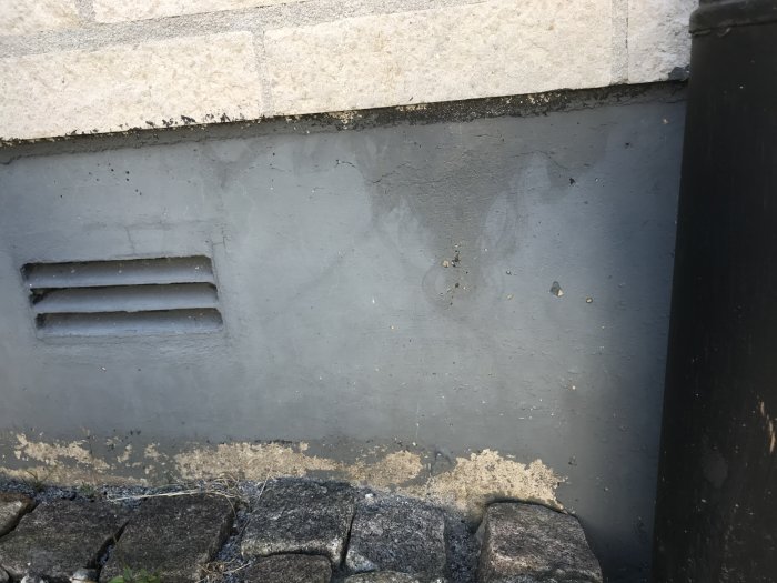Mörkt märke på grundmurens yta under kantsten, risken för fukt nära ventilationsspringa.