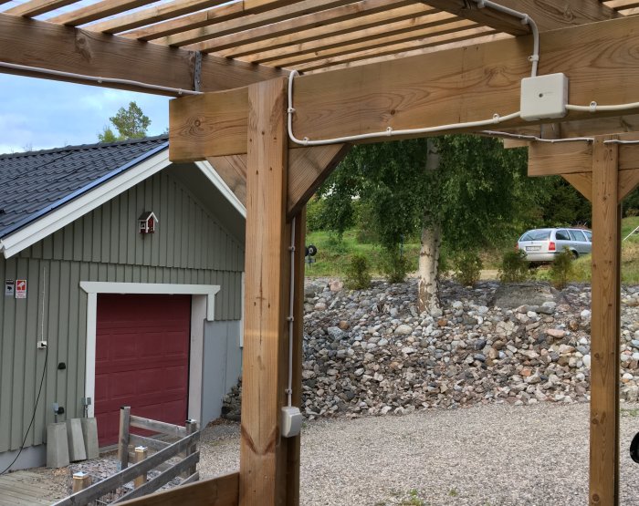 Kopplingsdosa monterad på träram för utebelysning vid ett hus, med grön fasad och röd garageport i bakgrunden.