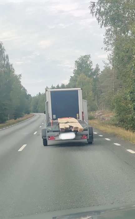 Lastbil på väg med osäkert säkrad last av brädor och spånplattor på flak bakom bil.