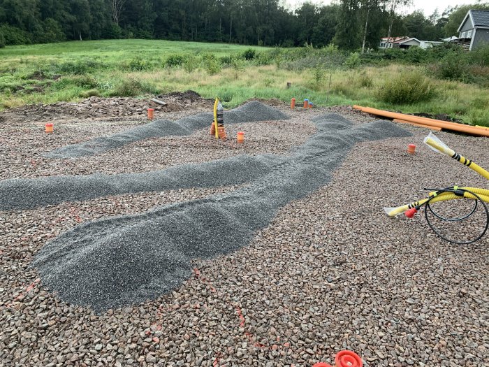 Högar av grus och flis utspridda för markarbete i en trädgård med verktyg och material synliga.