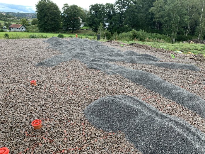 Påbörjade arbetet med att lägga ut grått flis på en grusbelagd yta utomhus med grönska i bakgrunden.