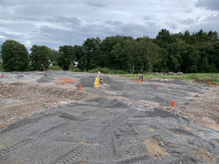 Byggplats med utlagd flisgrus och orange markörer för byggprojekt under molnig himmel.