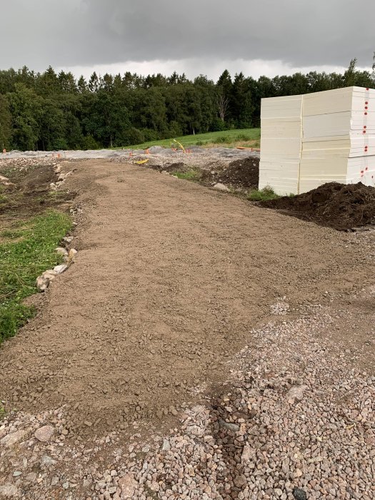 Nygrusad uppfart med 0/35-material intill en hög cellplast och en skog i bakgrunden under en molnig himmel.