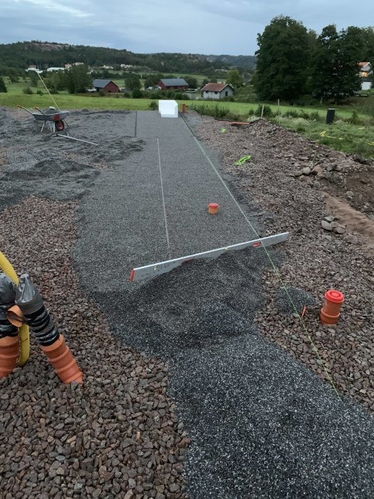 Nyutlagt flis på ett underarbete för en framtida entréväg, med en skottkärra och landskap i bakgrunden.