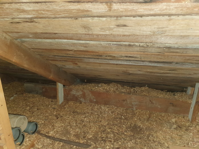 Takstolar ihopkopplade med balk på vind, avsaknad av stöd underifrån, med synlig spånskiva och rör på golvet.