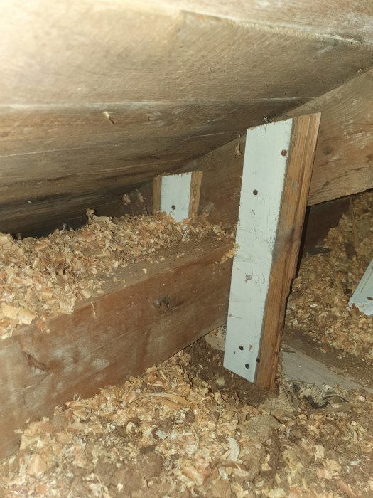 Konstruktion med balkar och klossar i takstolarna på en vind, omgivet av sågspån.