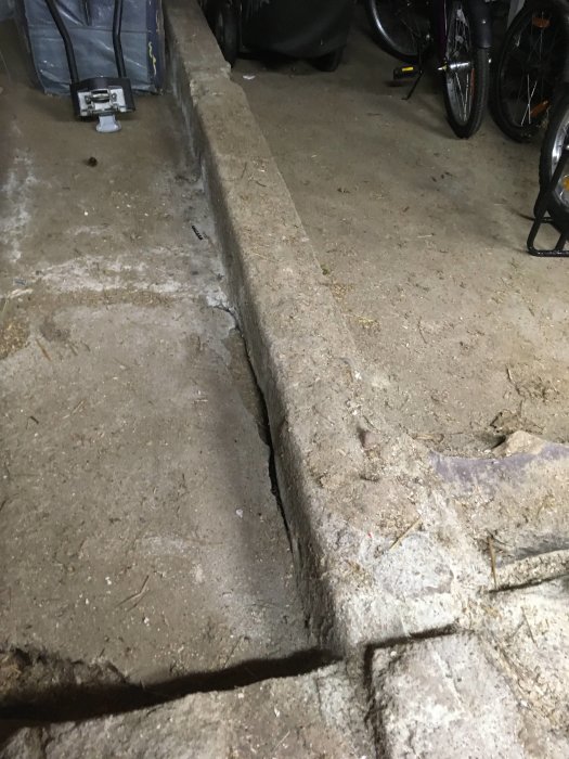 Ojämnt betonggolv med sprickor och håligheter i en ladugård, behöver renoveras.