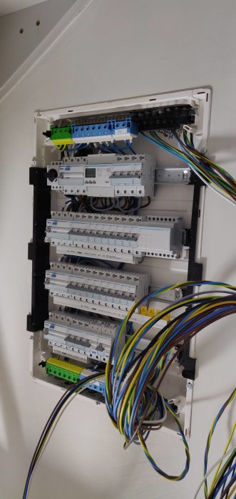 Öppen elcentral med flera brytare och kopplade kablar som hänger löst, under installation.