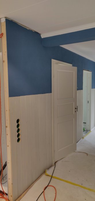 Renoverad hall med nyinstallerad pärlspont, dörr, foder och pågående elektrisk installation.
