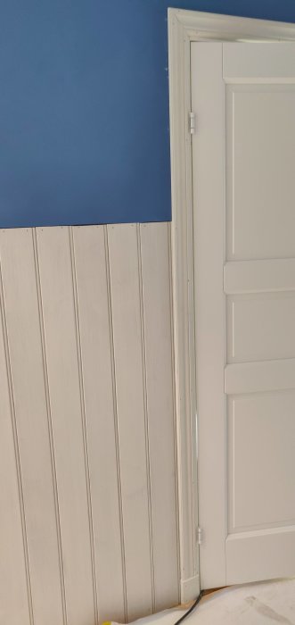 Nyinstallerad pärlspont och vit dörr med fodringar i en hall med blå vägg.
