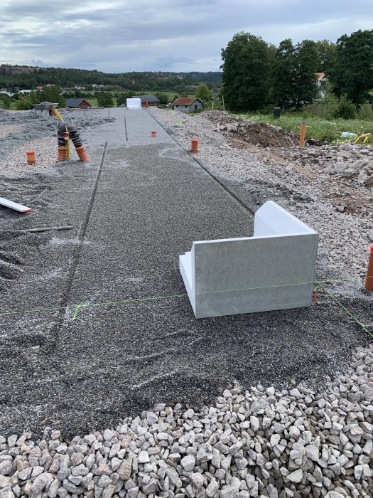 Nyplanerat byggeområde med borttagen flis, gruskross och markeringsrör på marken.