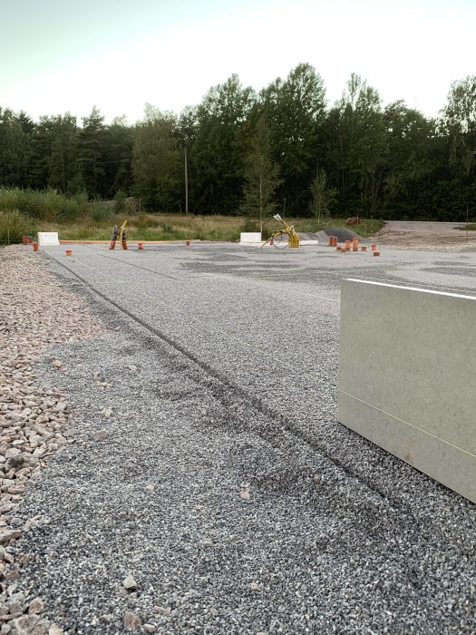 Renoverad grusyta utan flis med avgränsningskoner, cykel och skogsbakgrund.