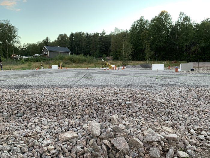 Tom byggplats med grusyta och avstängd arbetsområde i bakgrunden.