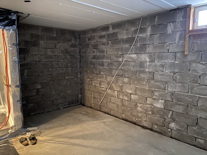 Ett hörn av en källare med bar murstensvägg och betonggolv, med spår av renoveringsarbete.