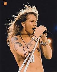 Man som sjunger i mikrofon med tatuerade armar, bar överkropp och långt hår.