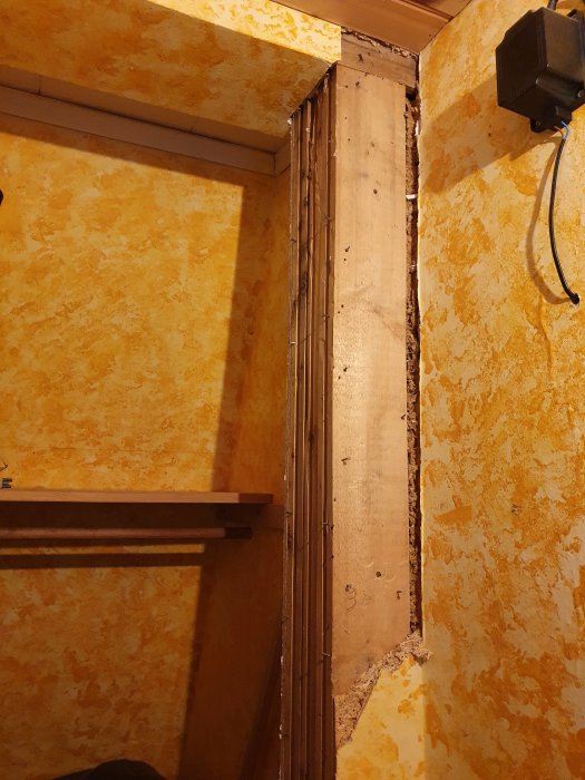 Oisolerad pelare i ett rum med orange tapet, där ytskiktet har börjat rivits bort, och pelaren verkar instabil.