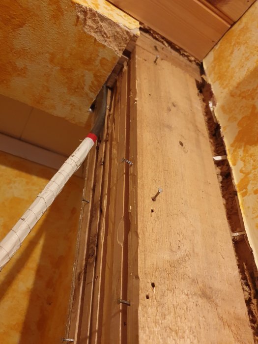 En pelare i en klädkammare med bortrivna ytskikt och synliga spikar, ej fast i balken ovanför.