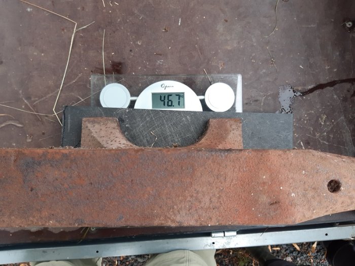 Ett gammalt städ som väger 46,7 kg på en digital våg, med fokus på dess rostiga yta och hål på sidan.