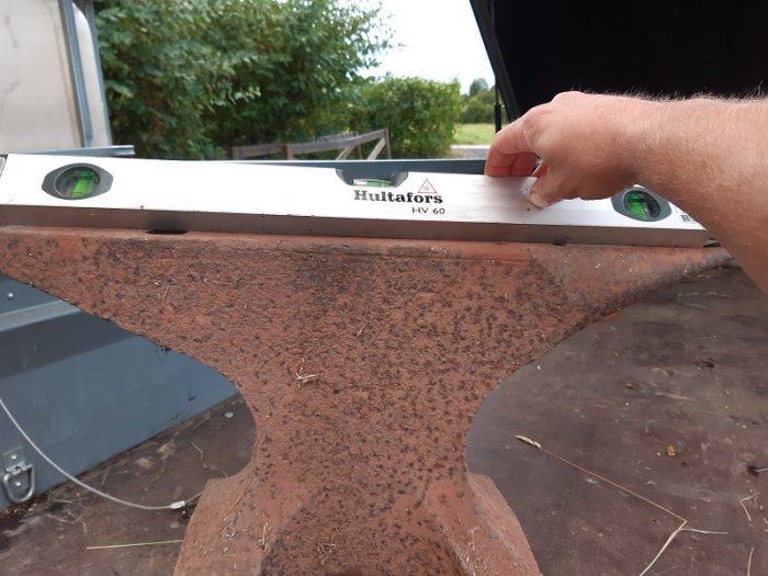 Närbild av ett använt städ med ett vattenpass ovanpå, hand som justerar vattenpasset.