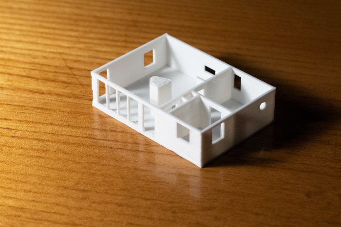 3D-printad miniatyrmodell av en stuga på ett träbord.