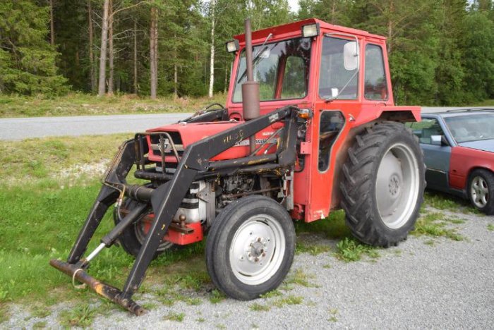 Röd traktor med frontlastare parkerad utomhus med skog i bakgrunden.