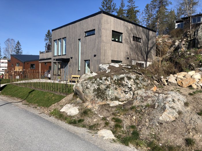 Moderna hus på 1760 kvm tomt under byggprocessen, med stenig trädgård och nyplanterade träd.