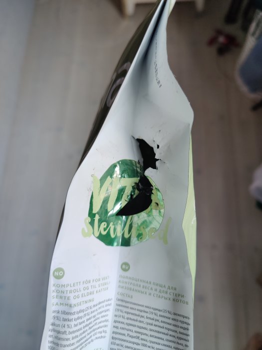 En upprivet förpackning av kattmat med ett stort hål som ser ut att vara söndertuggat eller uppätet.