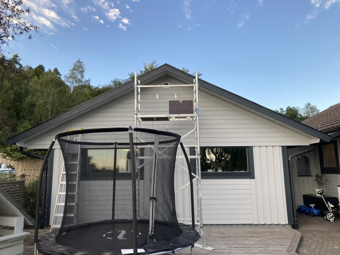 Husfasad med ny monterad plåt, och en ställning framför. Trampolin syns i förgrunden.