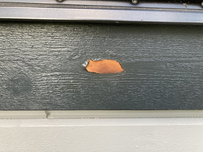 Bubbla i svart färg med synlig underliggande rödbrun plåt på en byggnad.