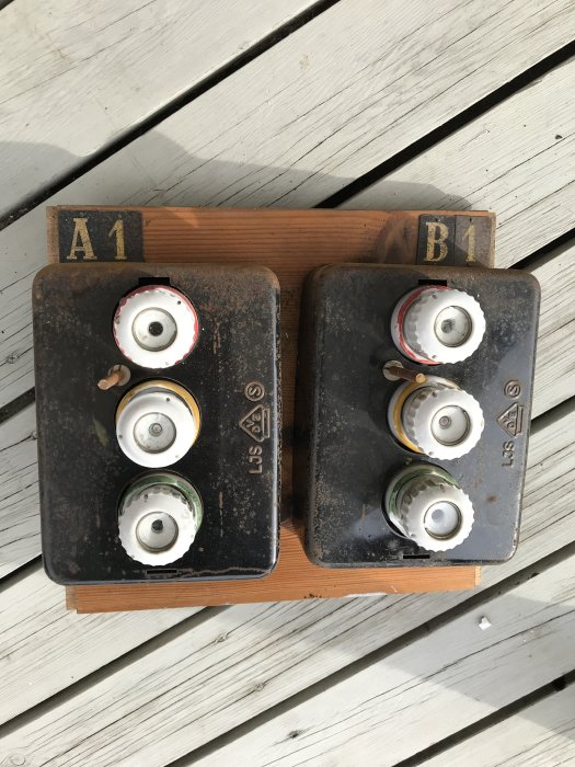 Gammalt proppskåp med keramiska proppar märkt "A1" och "B1" på träplatta, hittat på vind.