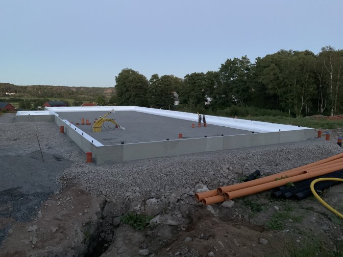 Grundläggning med utlagda kantelement och grus på byggplats i skymningen.