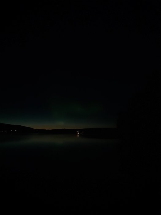 Norrsken över en mörk landskap med skymt av fullmånen och en svagt upplyst himmel.