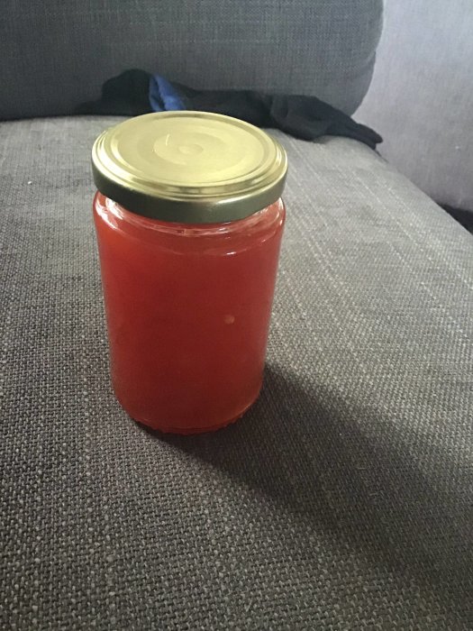 En burk med hemgjord röd marmelad på ett grått tygunderlag.