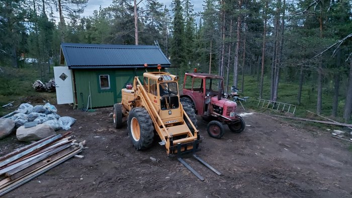 En BM Victor traktor med hytt från David Brown bredvid en lastare, i skogsmiljö vid en byggnad.