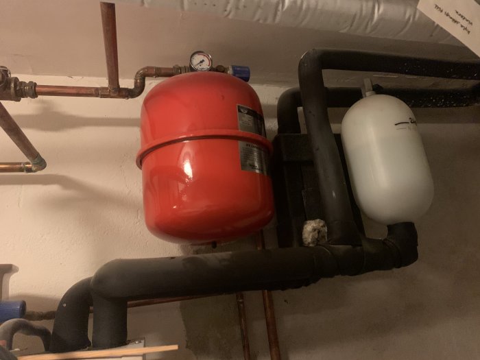 Installation av röd expansionskärl och vit trycktank ansluten till VVS-rör i ett utrymme.
