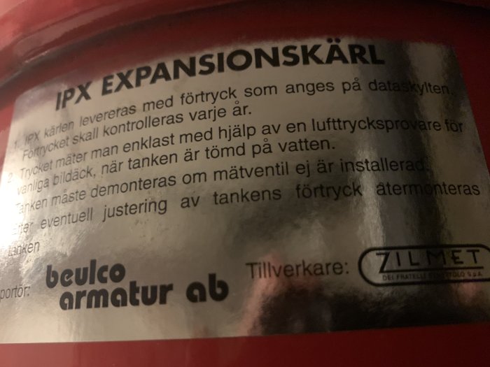 Informationsetikett på en röd expansionskärl med instruktioner och logotyper för Beulco Armatur och Zilmet.