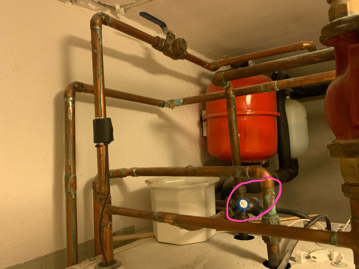 Värmesystem med kopparledningar och en rosa markerad manometer för tryckmätning.