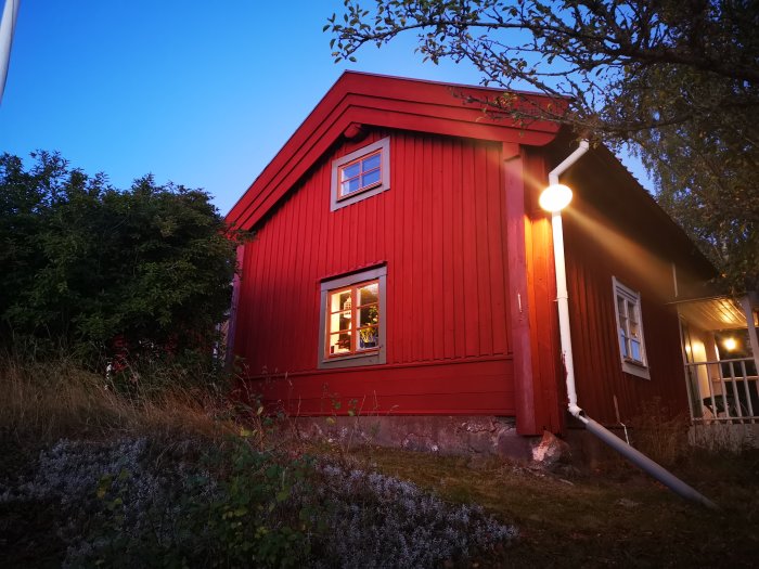 Rödmålat hus i skymningen med vita fönsterfoder och en vit avvattning.