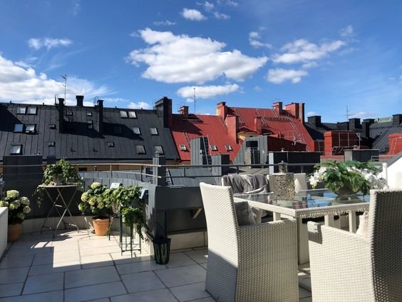 Terrass med utemöbler och utsikt över stadstak mot blå himmel.