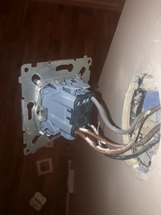 Eluttag med delvis inkopplade elektriska kablar i en vägg inför installation av dimmer.